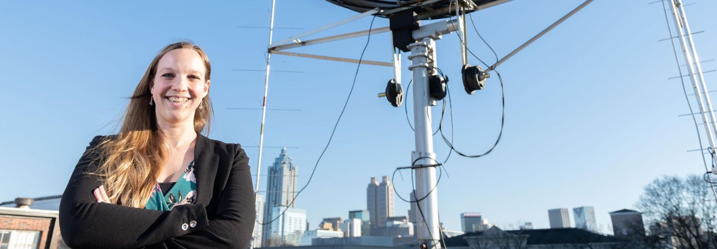 Mariel Borowitz on a rooftop, standing in front of a satellite. The Atlanta skyline is in the background.