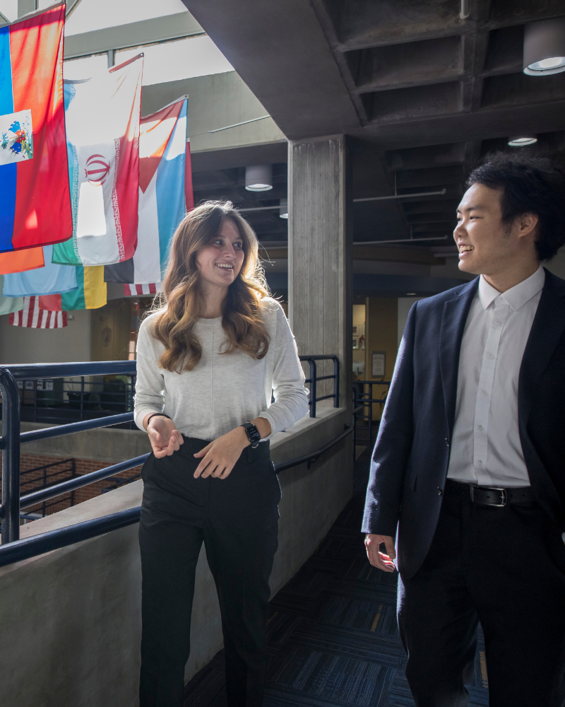 two students walking in front of flags