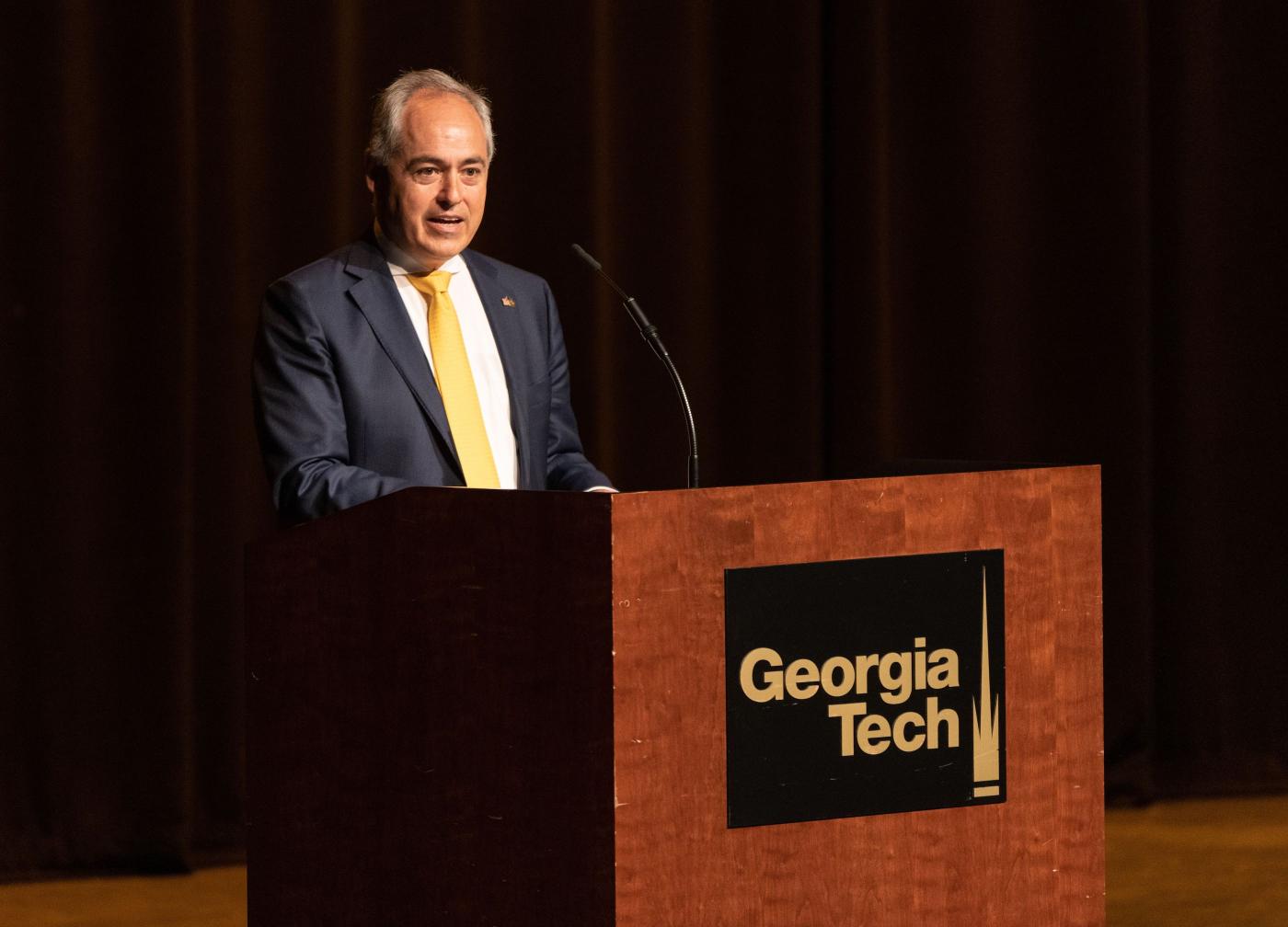 Ángel Cabrera stands at a lectern with a Georgia Tech logo on it to address an audience.