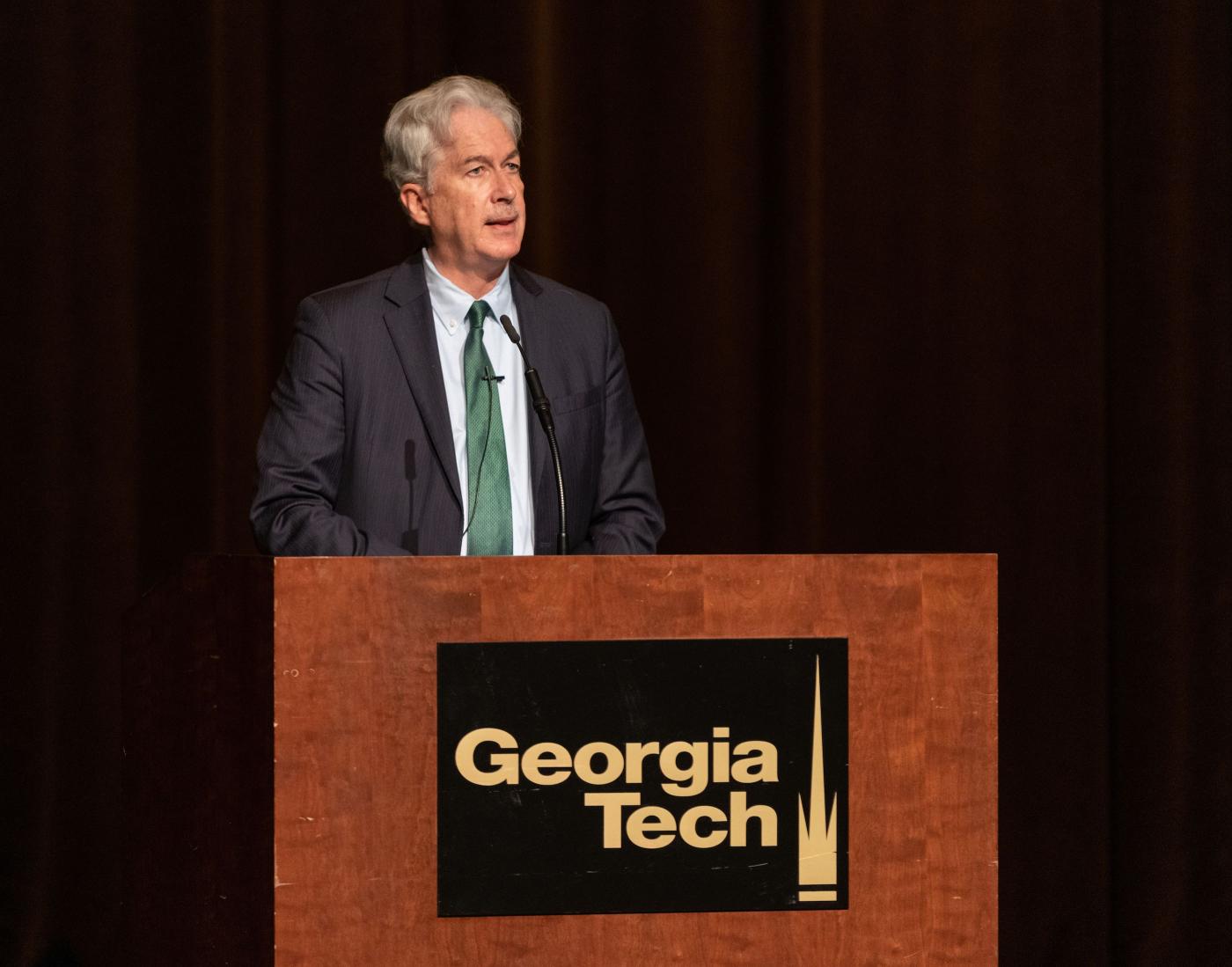 William Burns stands at a lectern with the Georgia Tech logo on it and addresses an audience.