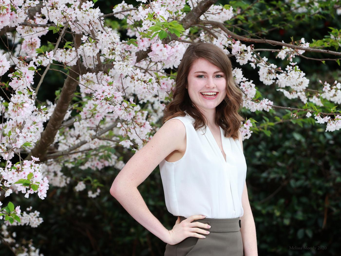 Kayli Moody poses in front of a white/pink flowering tree.
